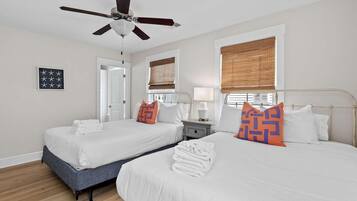 A hotel room with two beds, a ceiling fan, a window with blinds, a bedside table with a lamp, and a framed picture on the wall.