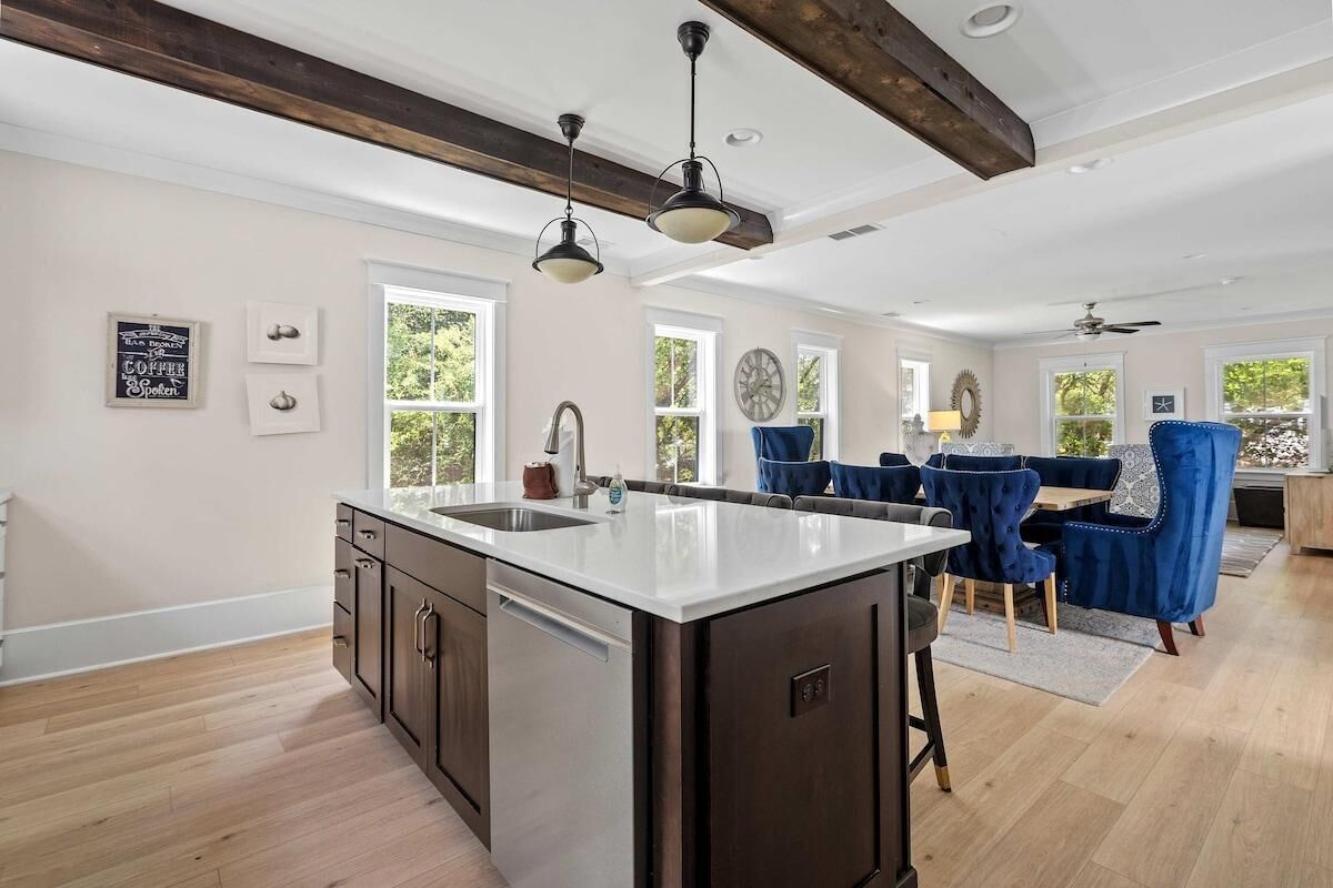 A spacious kitchen with a large island, wooden beams, and a dining area with blue chairs.
