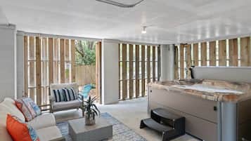 A modern outdoor living area with a hot tub, seating, and a view through wooden slats.