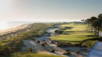 Ein Golfplatz an der Küste mit einem Sandweg, grünen Spielbahnen und einem Strand im Hintergrund.