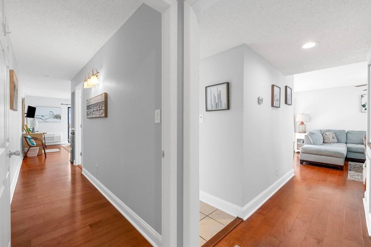 A hallway with wooden flooring, white walls, and a gray sofa in the background.