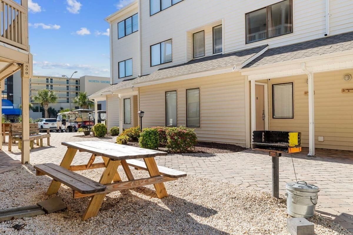 A patio area with a picnic table, a barbecue grill, and a gravel ground.