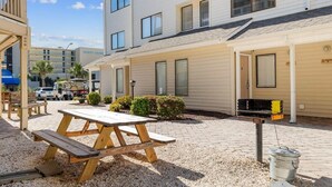 A patio area with a picnic table, a barbecue grill, and a gravel ground. - Magic Myrtle, On the Beach, Pet Friendly (Myrtle Beach)
