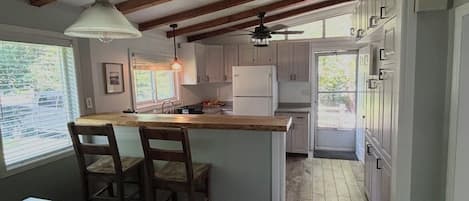 Una cocina con vigas de madera, una isla central con taburetes de bar, un refrigerador y un ventilador de techo.