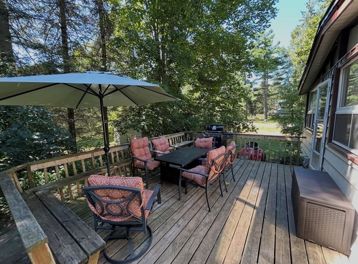 Una terraza de madera con mobiliario exterior, incluyendo una mesa y sillas, y un paraguas grande.