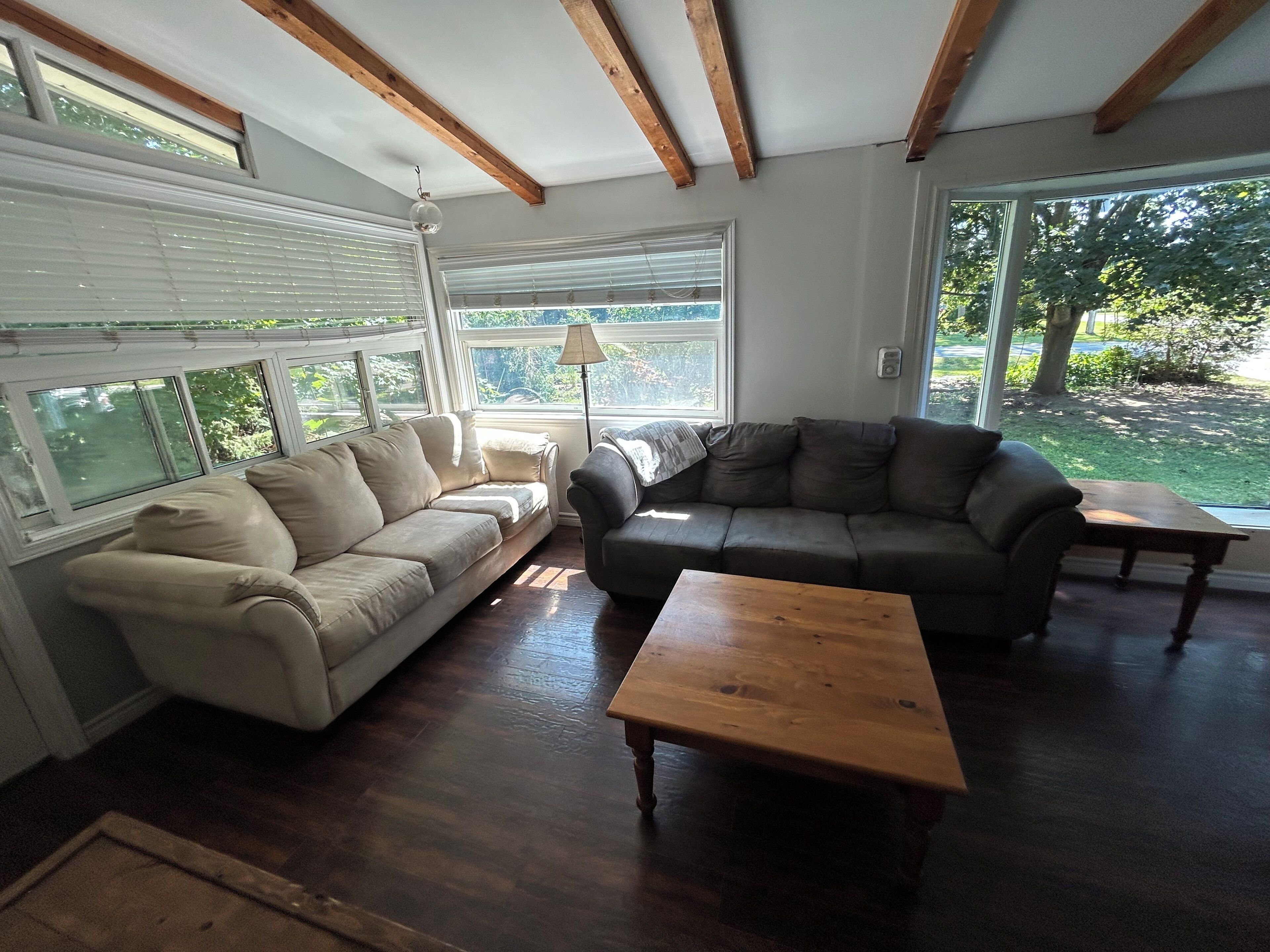 Una sala de estar con dos sofás, una mesa de centro de madera y ventanas grandes con persianas.