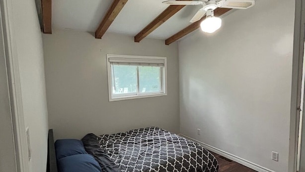 A bedroom with a bed, a window, a ceiling fan, and wooden beams.