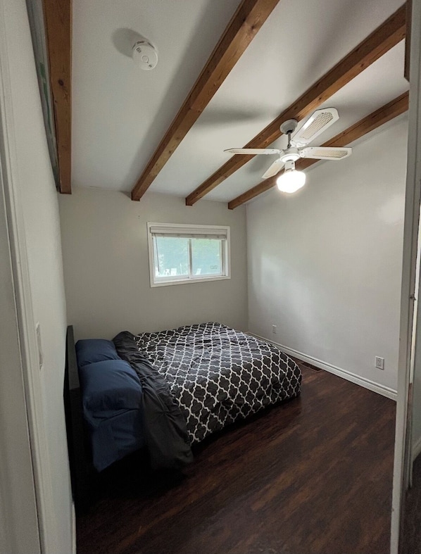 Une chambre à coucher avec un lit, une fenêtre, un ventilateur de plafond et des poutres en bois.