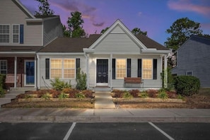 A two-story house with a front porch, a small front yard with plants, and a driveway. - The Suite Carolinas (Charleston)
