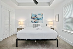 A bedroom with a bed centered in the room, flanked by two bedside tables with lamps, a large abstract painting above the bed, and a window with blinds on the right. - Penny Lane, Park Circle, 15m Dwtn CHS (North Charleston)