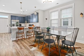 A modern kitchen with dark blue cabinets, a white countertop, and a dining area with a large table and chairs. - Penny Lane, Park Circle, 15m Dwtn CHS (North Charleston)