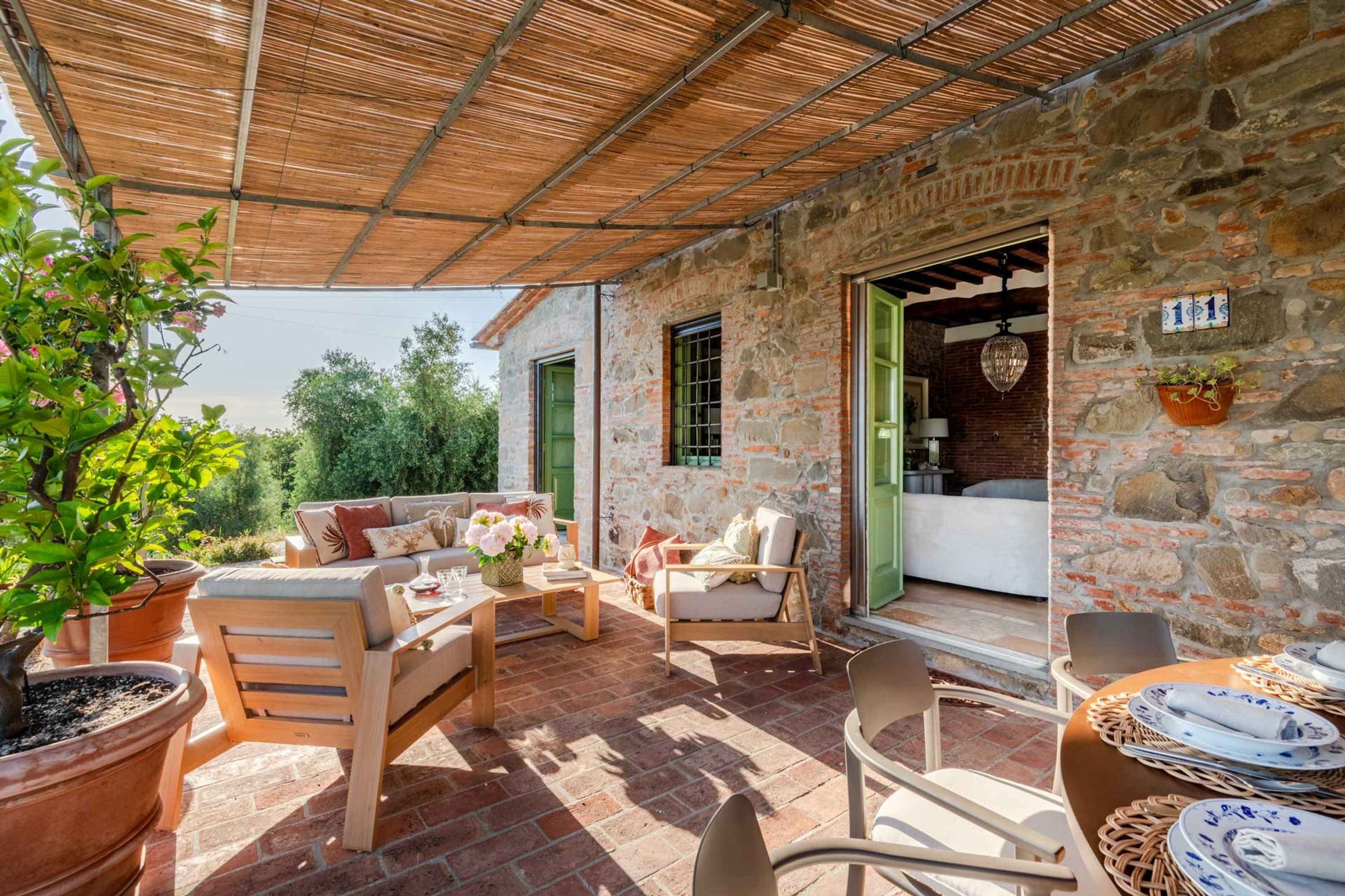 A covered patio with stone walls, outdoor furniture, and potted plants.