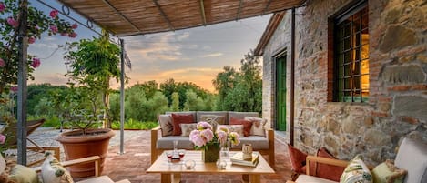 A covered outdoor seating area with a stone wall, a sofa, and a table set for dining.