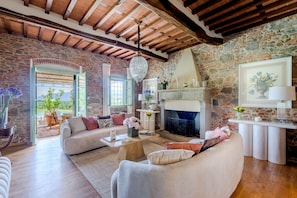 A spacious living room with a stone wall, a fireplace, and a view through a large window. - Villa Pellegrini in Montecarlo (Montecarlo)