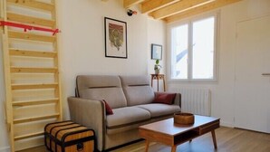 A room with a sofa, a table, a wooden floor, a window, and a radiator. - Charming apartment in Rezé near Sèvre (Rezé)