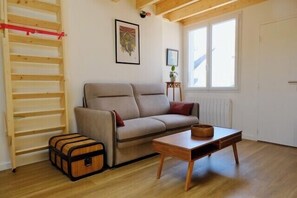 Ein Zimmer mit einer Couch, einem Tisch, Holzboden, einem Fenster und einer Heizung.