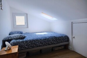 Ein kleines Zimmer mit einem Einzelbett, einem Oberlicht, einem Fenster und einer Tür.