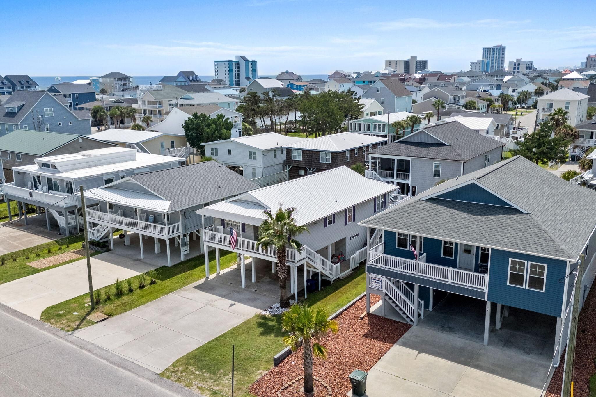 Un barrio residencial con varias casas de dos pisos, algunas con porches anexos y una vista despejada del océano al fondo.