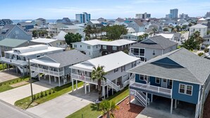 Un quartier résidentiel composé de plusieurs maisons à deux étages, dont certaines sont dotées de vérandas et offrent une vue dégagée sur l’océan en arrière-plan.