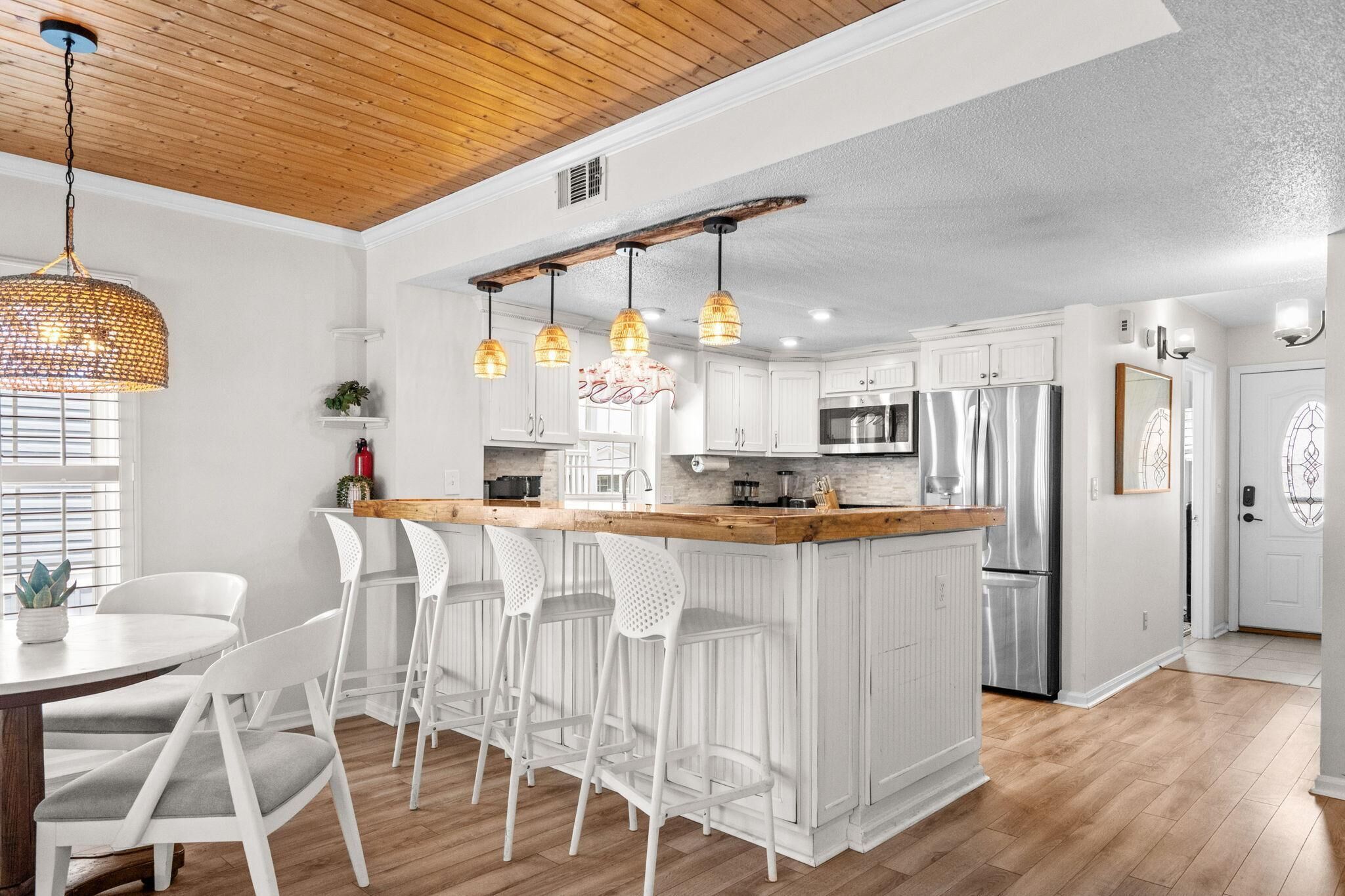 A modern kitchen with white cabinetry, a wooden ceiling, and a bar area with white stools.