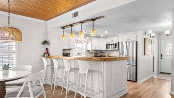 A modern kitchen with white cabinetry, a wooden ceiling, and a bar area with white stools.
