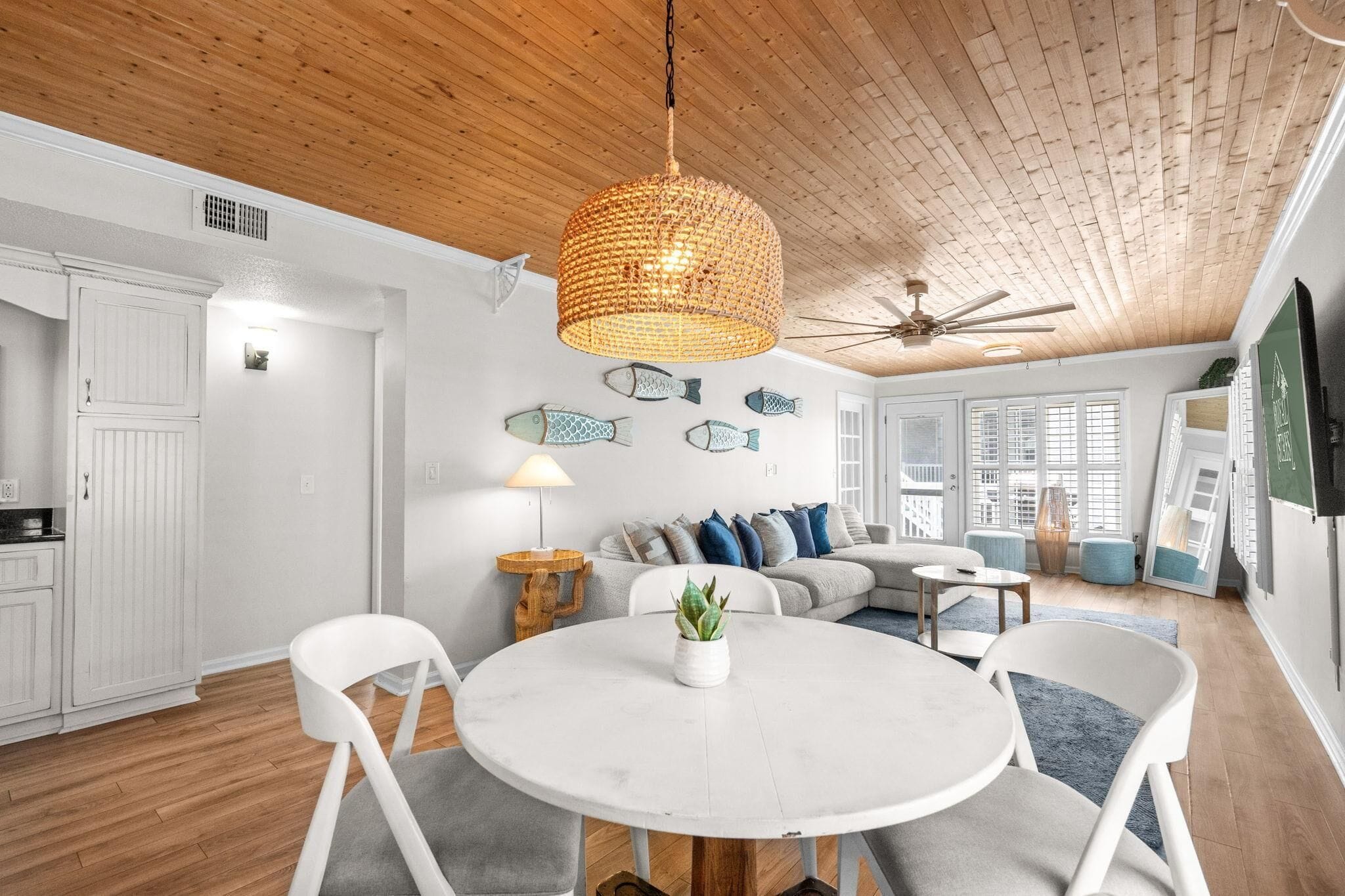 A modern interior with a round dining table, white chairs, a ceiling fan, and a woven light fixture.