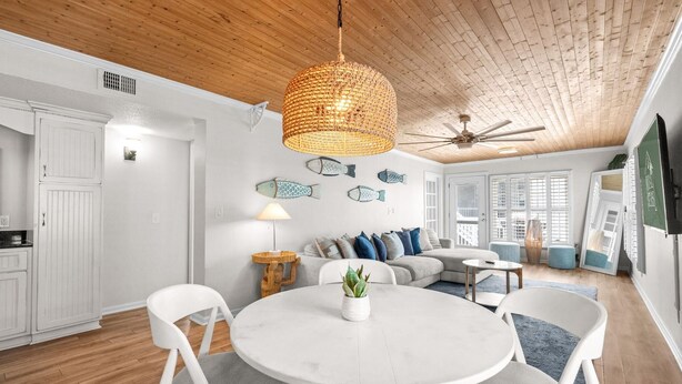 Un intérieur moderne avec une table de salle à manger ronde, des chaises blanches, un ventilateur de plafond et un luminaire en matière tressée.