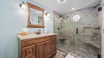Une salle de bain avec un meuble-lavabo en bois, un grand miroir et une douche séparée par des parois en verre.
