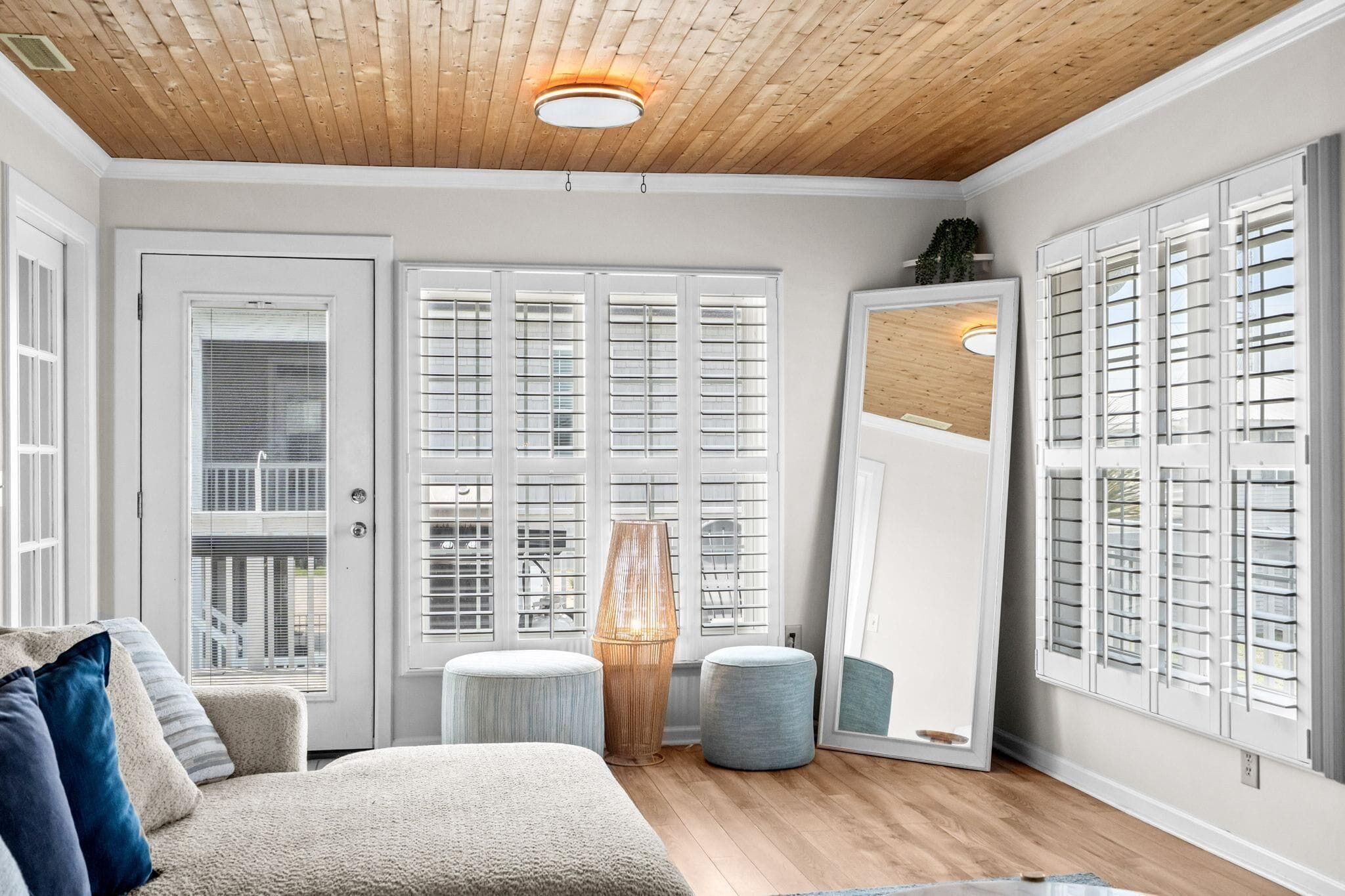 A room with a wooden ceiling, large windows with shutters, a sofa, and a mirror.