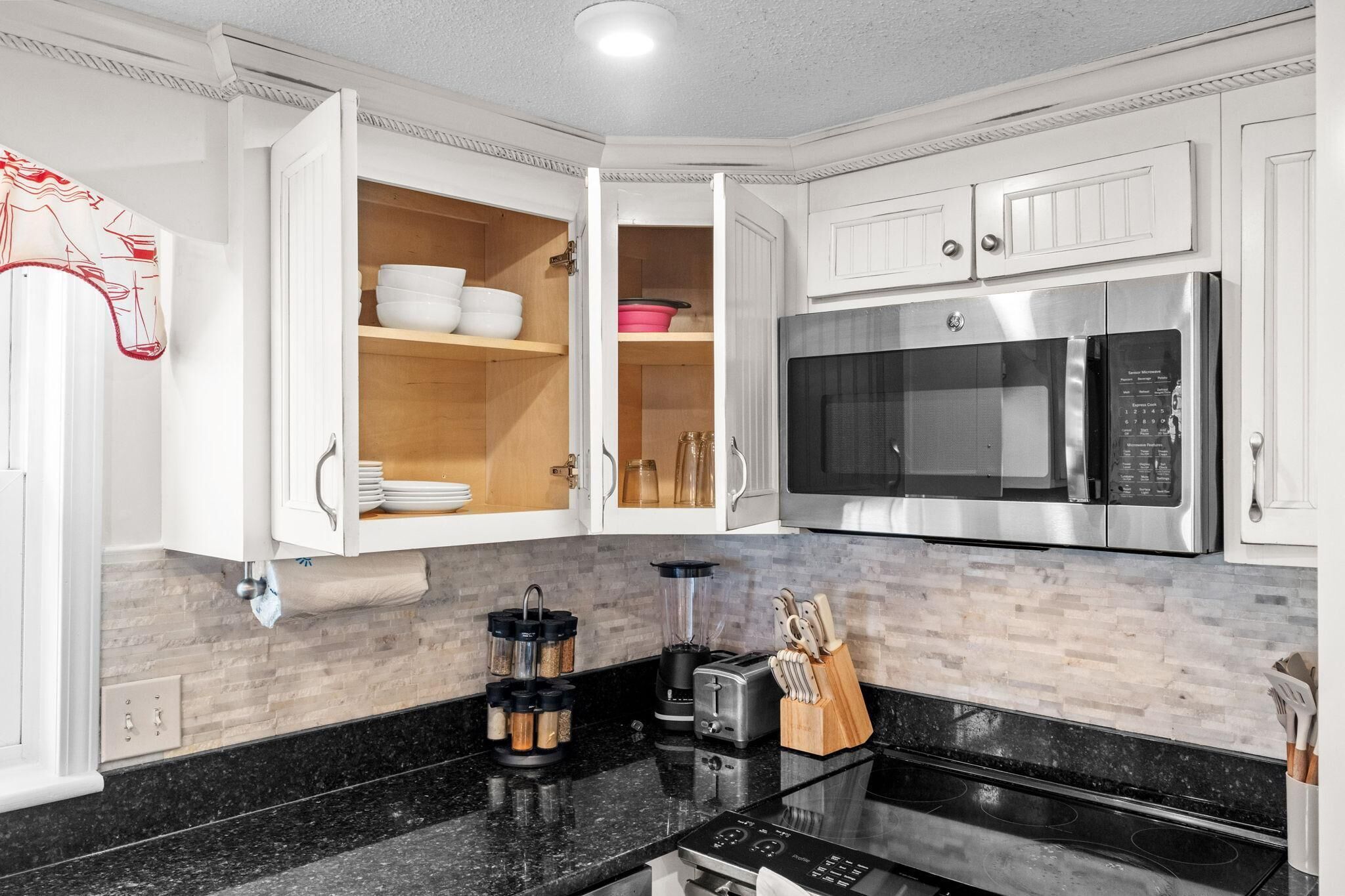 A modern kitchen with white cabinetry, a stainless steel microwave, a blender, and a toaster.
