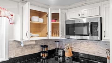A modern kitchen with white cabinetry, a stainless steel microwave, a blender, and a toaster.