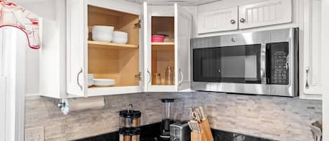 A modern kitchen with white cabinetry, a stainless steel microwave, a blender, and a toaster.