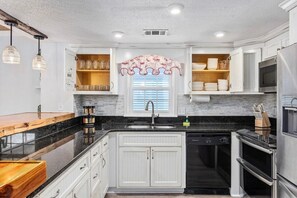 A modern kitchen with white cabinetry, a black countertop, a built-in dishwasher, a microwave, and an oven. - Grove Cove - 1'5 Blocks From Beach- Dog Friendly (North Myrtle Beach)