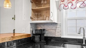 Une cuisine équipée d’un appareil à café intégré, d’un meuble pour ranger les verres à vin et d’une fenêtre avec des rideaux.