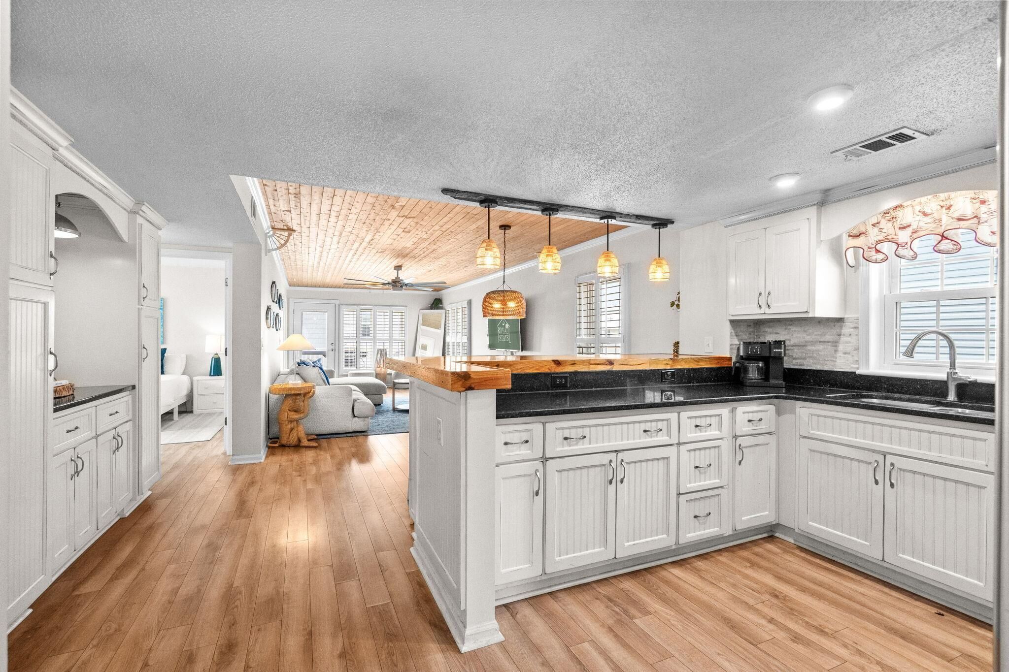 A spacious kitchen with wooden flooring, white cabinetry, and pendant lighting.