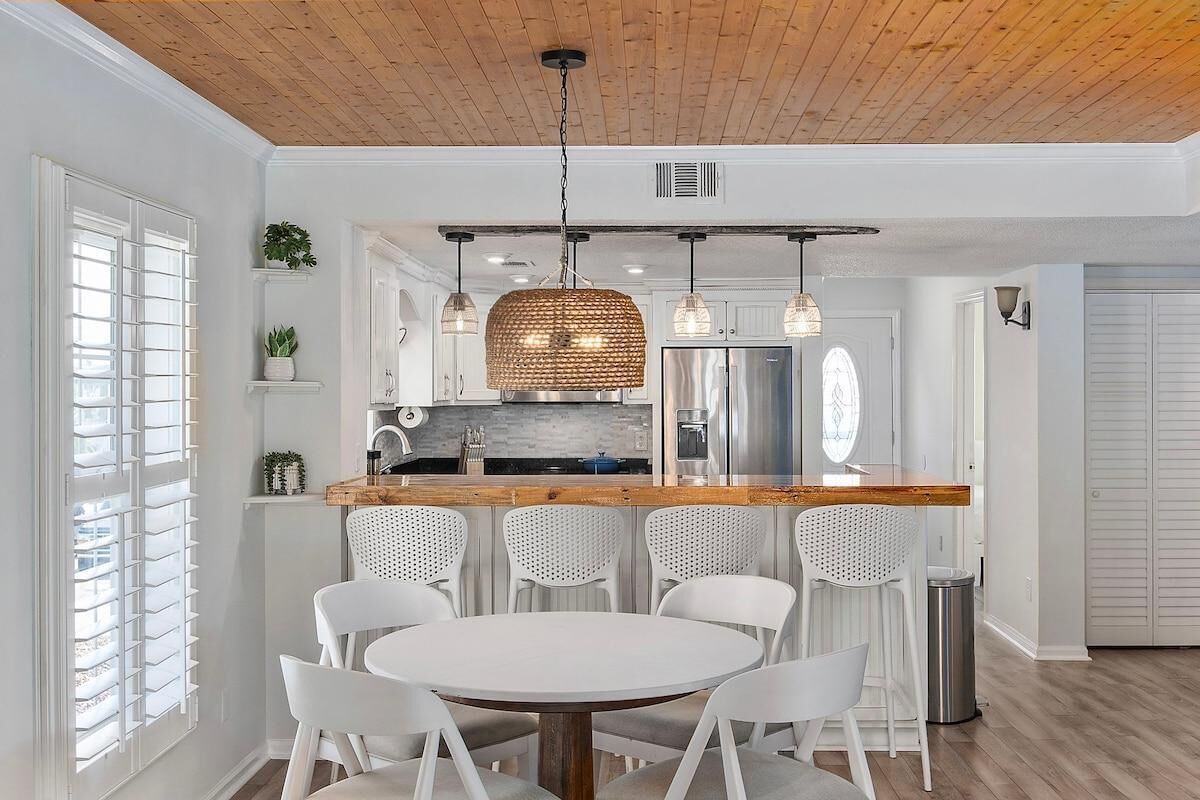 A modern kitchen with white cabinetry, a wooden countertop, and a hanging woven light fixture.
