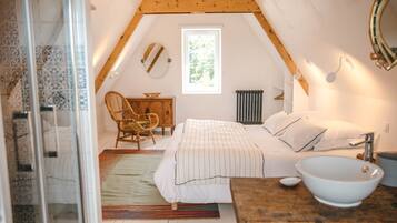 Un dormitorio con una cama, una silla de madera, una mesita de noche con un cuenco, una ventana y un radiador.