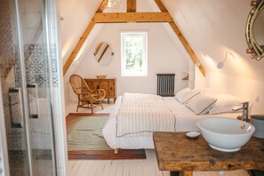 Un dormitorio con una cama, una silla de madera, una mesita de noche con un cuenco, una ventana y un radiador.
