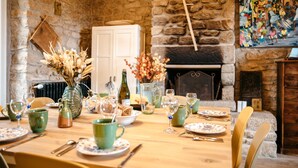 Mesa de comedor decorada con vajilla verde, un jarrón con flores secas y una chimenea en una habitación con paredes de piedra.