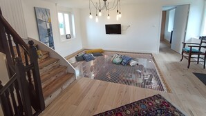 Un espacio habitable espacioso con una escalera, un televisor montado en la pared y un tapete estampado en el suelo.