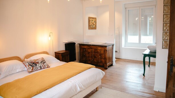 Un dormitorio con cama, mesitas de noche, cómoda, ventana con persianas y una obra de arte colgada en la pared.