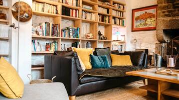 Un salon chaleureux avec un canapé en cuir noir, une bibliothèque en bois remplie de livres, une cheminée en pierre et un tableau accroché au mur.