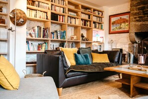 A cozy living room with a black leather sofa, a wooden bookshelf filled with books, a stone fireplace, and a painting on the wall.