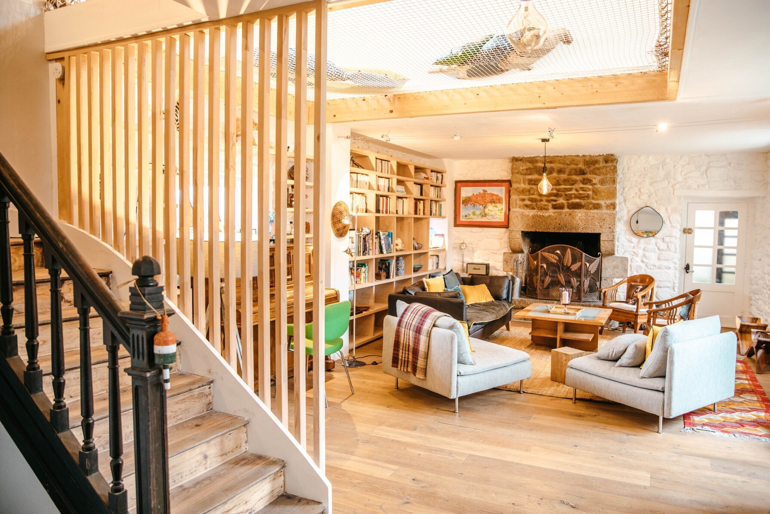 Un salon spacieux doté d’une cheminée, d’un escalier avec des rampes en bois et d’une bibliothèque remplie de livres.