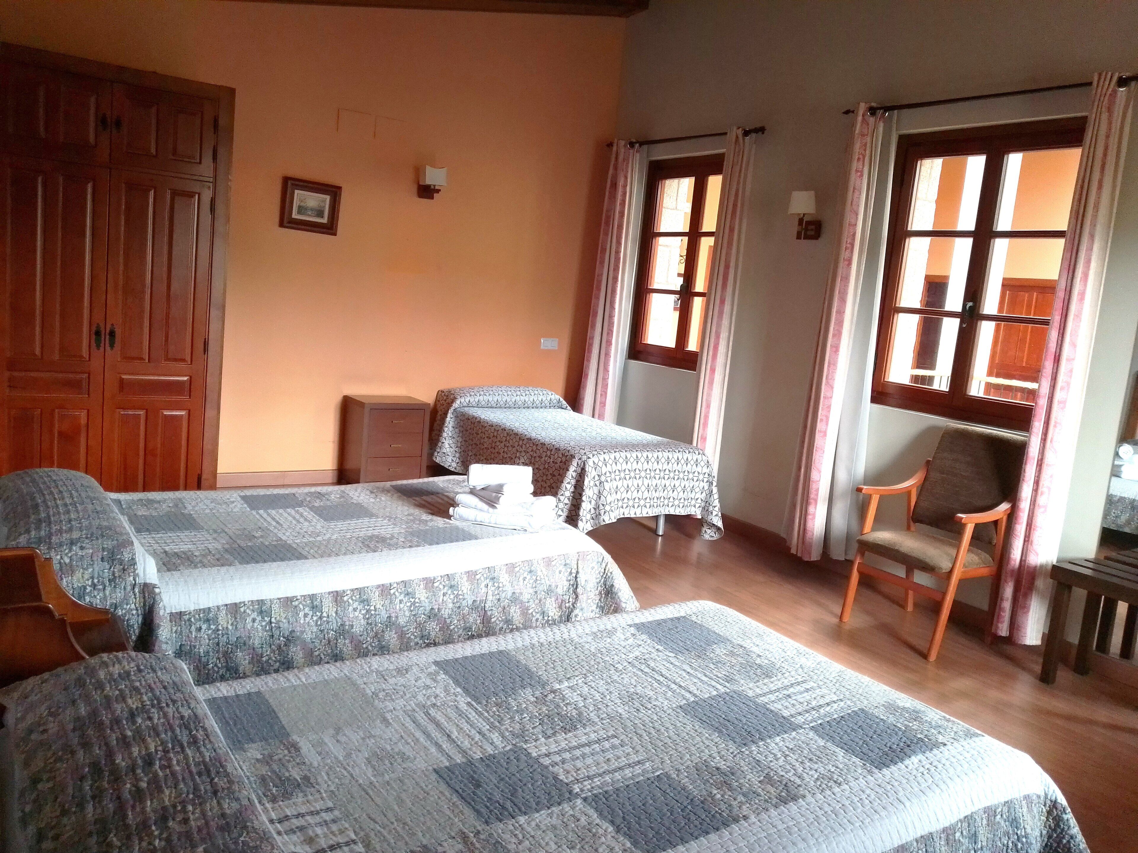 A hotel room with two beds, a wooden wardrobe, a desk, and a chair.