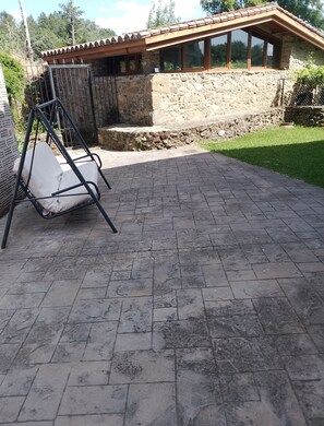 A patio with a swing chair, stone walls, and a wooden structure with windows.