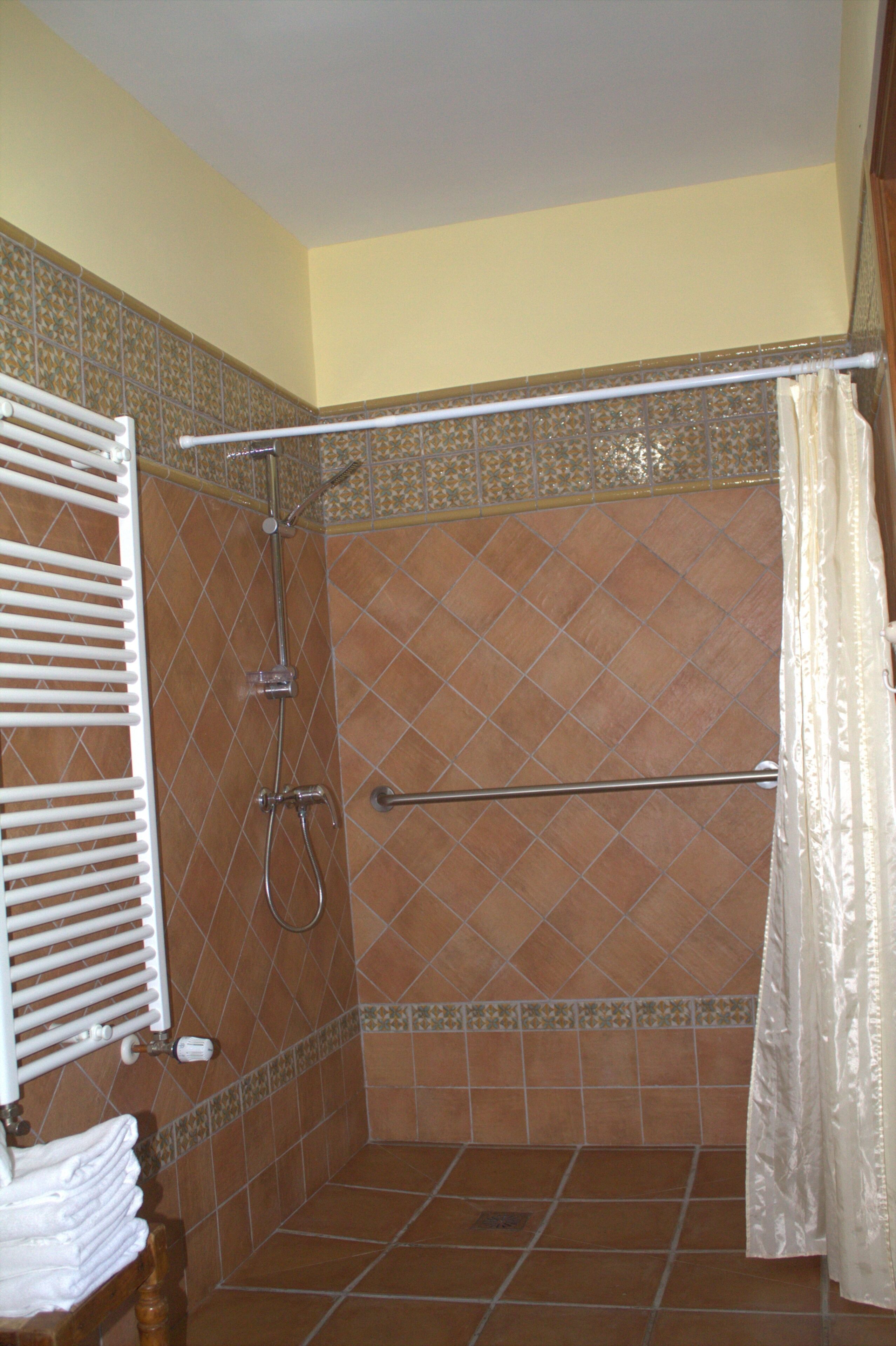 Un espace douche avec un mur carrelé, un porte-serviettes blanc et un rideau de douche.