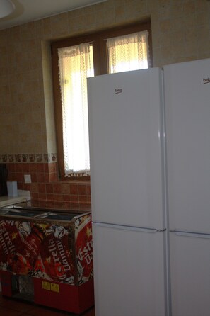 A kitchen with a refrigerator, a window with lace curtains, and a tiled backsplash.