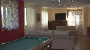 A living room with a pool table, a sofa set, a television, and a chandelier.