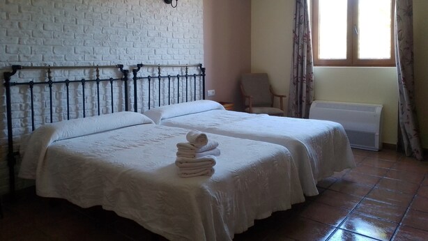 A room with two beds, a brick wall, a chair, and a window with curtains.